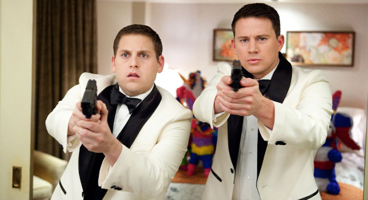Still from the movie "21 Jump Street" with Jonah Hill and Channing Tatum in white tuxes with guns drawn