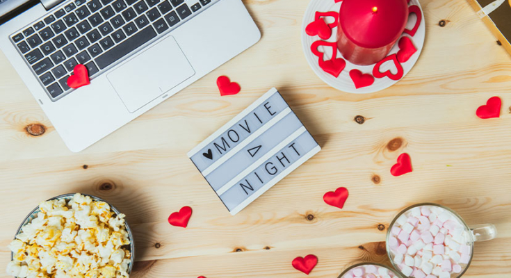 Laptop, popcorn, hot cocoa, candle and more set up for Valentine's movie date