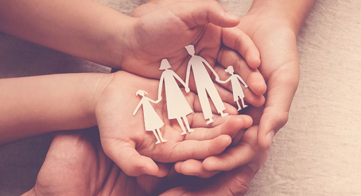Adult and children's hands holding paper cut outs of a family of 4