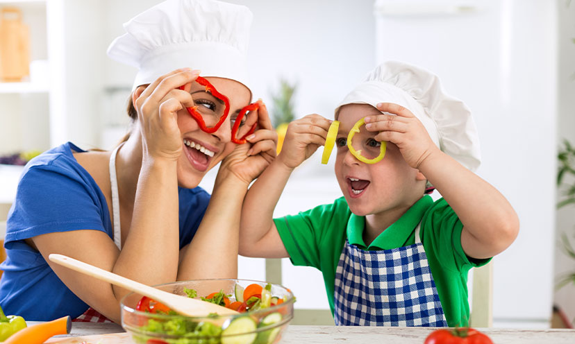 Woman and child in chef's hats holding bell peppers over their eyes like glasses