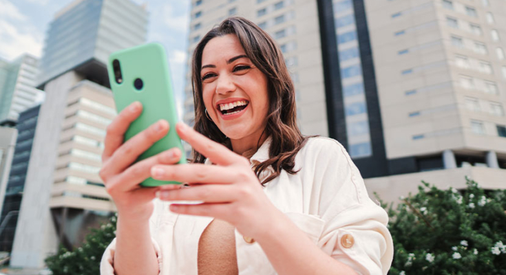 Woman smiling happily at smartphone outside