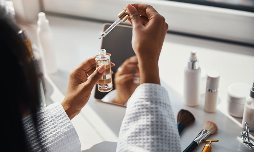 Woman's hands with a serum container and eyedropper with other skincare products in the background