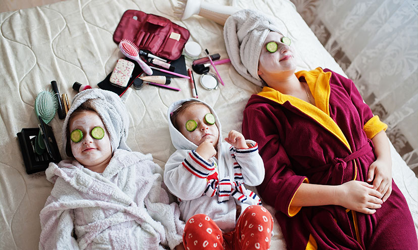 Parent and kids in face masks and robes with cucumbers on their eyes for spa day