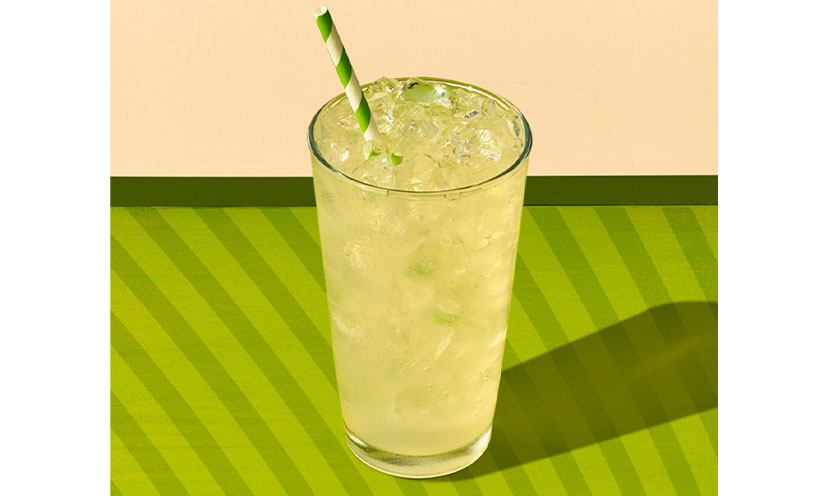 Pickle lemonade in a glass with a green striped straw on a green striped background