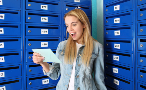 Excited woman holding piece of mail near mailboxes