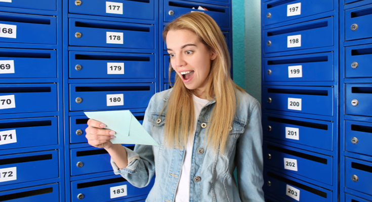 Excited woman holding piece of mail near mailboxes