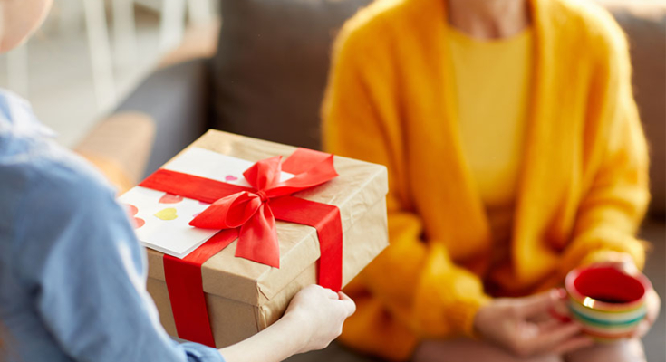 Child handing gift and card to woman with tea mug