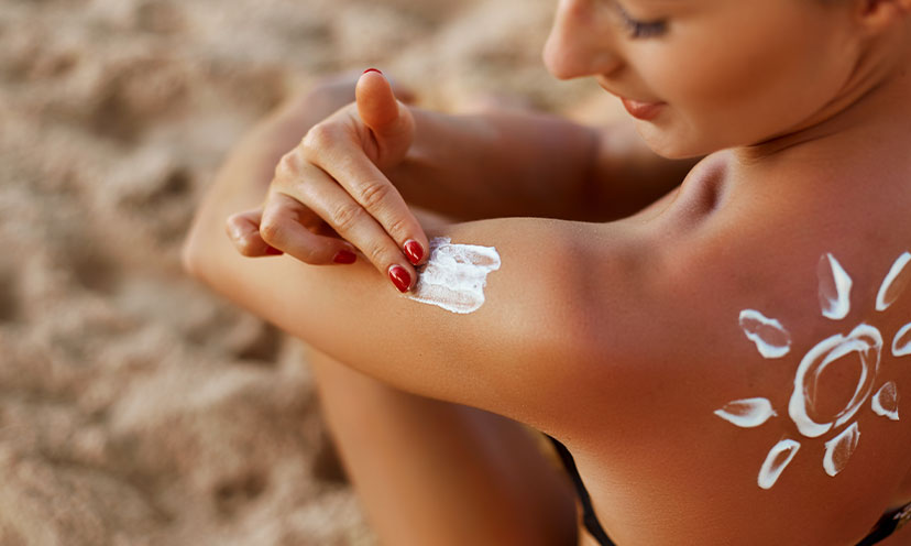 Woman applying sunblock with a sun drawn in sunblock on her back