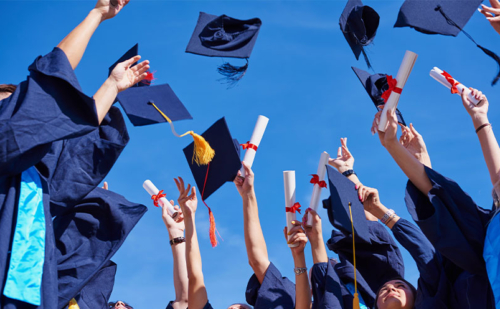 Graduates in dark blue robes tossing their caps into the air while some hold up rolled diplomas