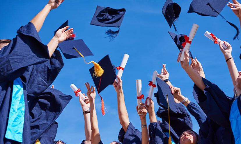 Graduates in dark blue robes tossing their caps into the air while some hold up rolled diplomas