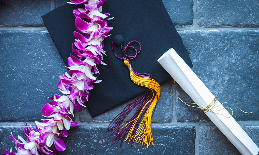 Graduation cap, diploma rolled up, and a flower lei across it 