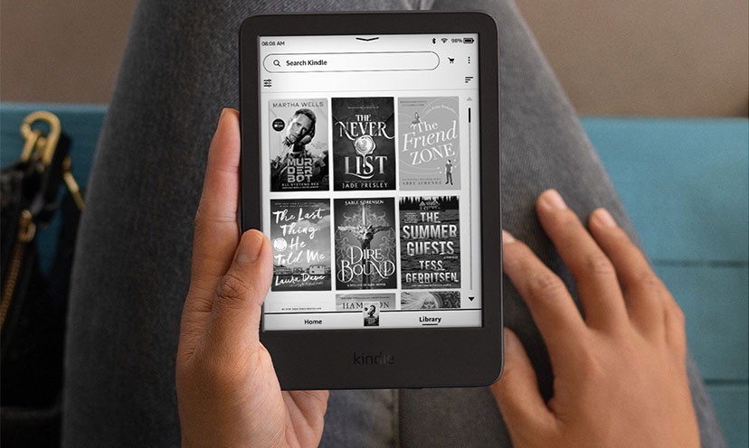 Picture of a Kindle e-reader on someone's lap with one hand holding it 